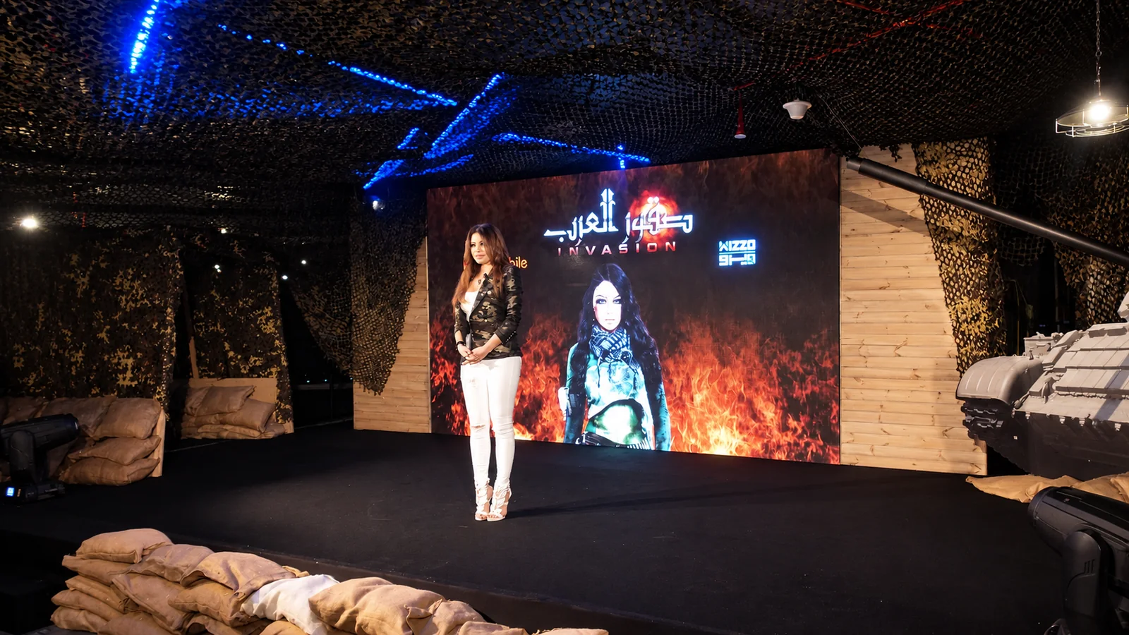 Presenter on the Invasion game launch stage in front of the camouflage-netted military set