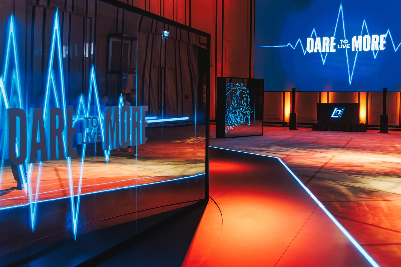 Neon pulse-line installation and Dare to Live More screen in the red-lit ballroom