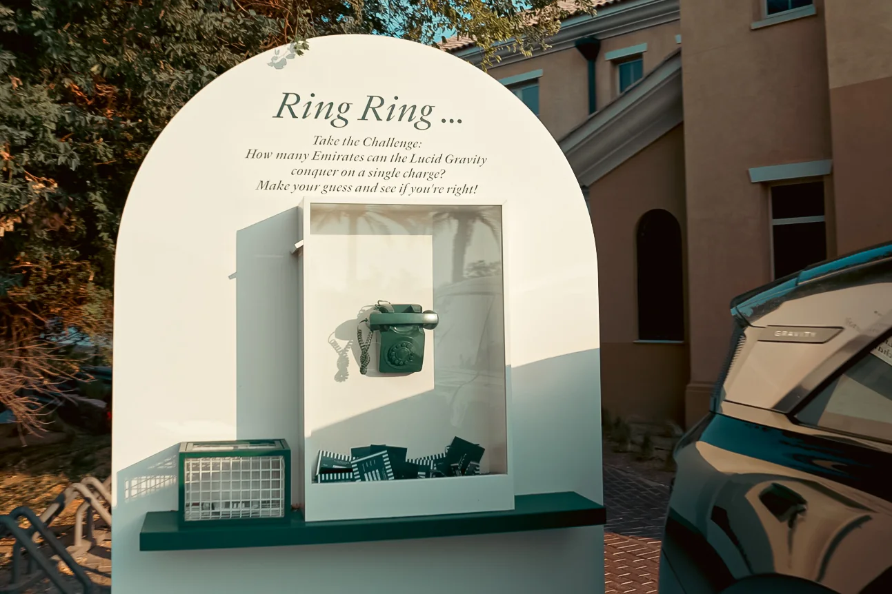 Arched Ring Ring challenge sign with a green telephone asking how many Emirates the Lucid Gravity can conquer on a charge