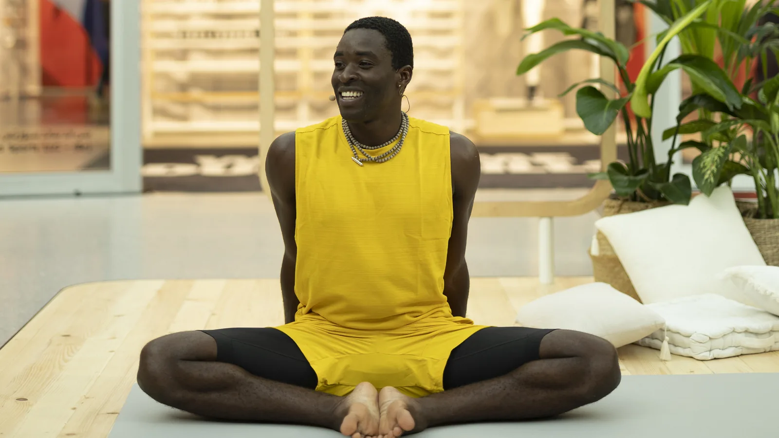Yoga instructor in yellow seated cross-legged on the wooden stage
